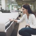 A woman chooses a mattress in a store. She sits next to him and examines him