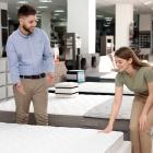 Young salesman helping customer to choose new modern orthopedic mattress in store